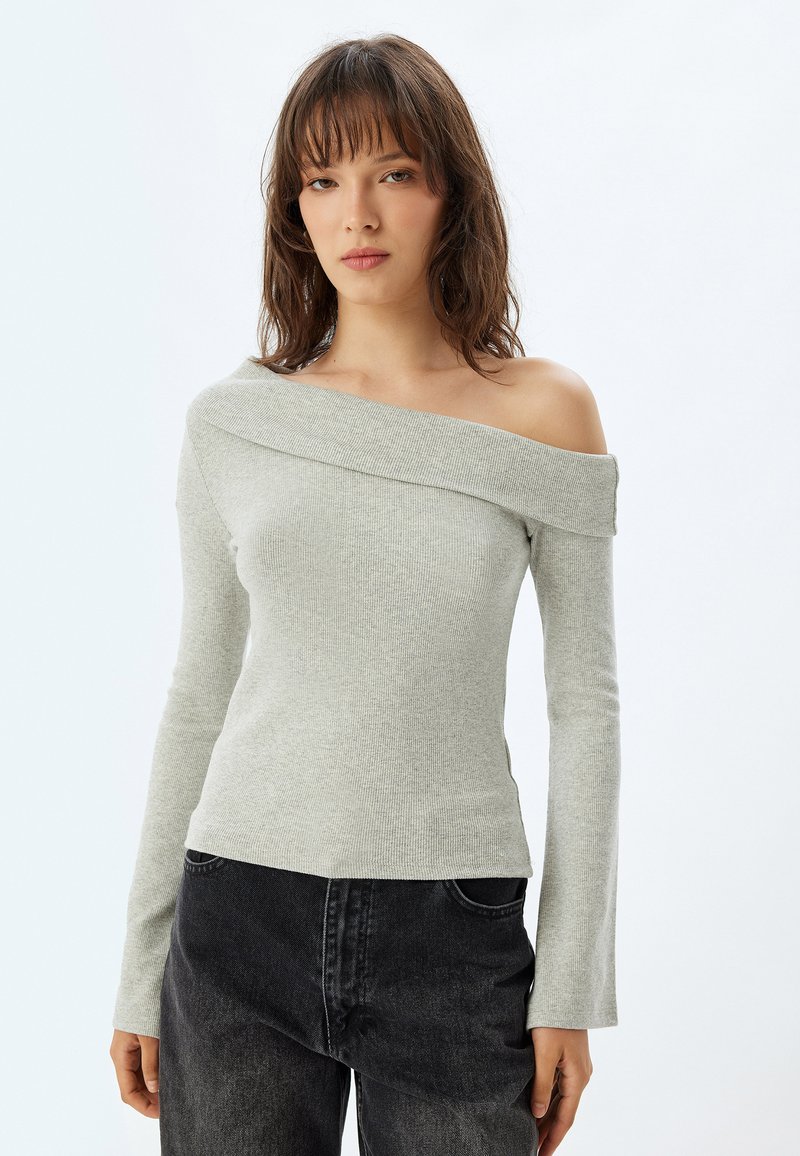 Lichtgrijze off-the-shoulder trui in een ribbelstructuur met lange mouwen, gecombineerd met donkergrijze denim. Eenvoudig, modern ontwerp.