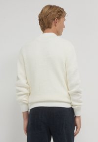 Maglione lavorato a maglia di colore crema con un motivo testurizzato, polsini e vita a costine. Il retro presenta un collo rotondo e un design a vestibilità comoda.