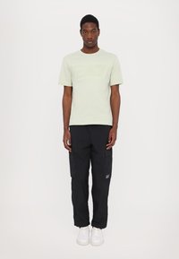 T-shirt vert clair à manches courtes avec logo "EA7" en relief, associé à un pantalon cargo noir avec poches et des baskets blanches.