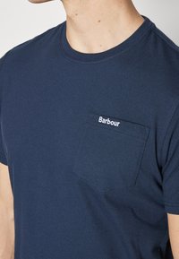 Granatowa bawełniana koszulka z okrągłym dekoltem, krótkimi rękawami i kieszonką na piersi z białym haftem logo "Barbour".