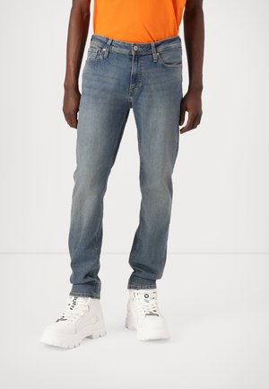 Lyseblå denimjeans med rett snitt, fem lommer og synlige sømmer, kombinert med hvite chunky sneakers.