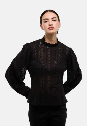 Blouse en dentelle noire avec manches bouffantes, encolure arrondie et motifs brodés complexes. Tissu texturé présentant des découpes.