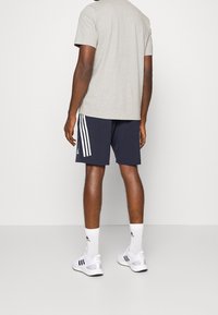 Grå kortärmad t-shirt kombinerad med marinblå shorts med vita sidostråk. Modell som bär vita strumpor och sportskor med svarta accenter.