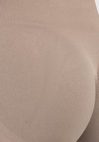 Beige naadloze leggings met een geribde textuur, voorzien van een gladde afwerking en een aansluitend ontwerp dat de rondingen benadrukt.