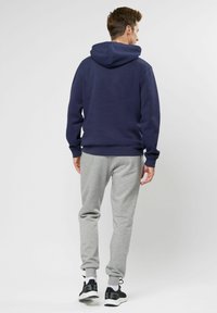 Sudadera azul marino con un bolsillo trasero, combinada con pantalones de chándal grises y zapatillas deportivas negras. La tela parece suave y con textura.