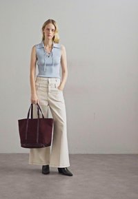 Top senza maniche a coste di colore azzurro chiaro con colletto, pantaloni beige a gamba larga, stivali neri con tacco e una borsa a tracolla di un rosso scuro con doppi manici.