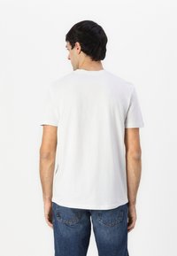 Hvit bomull T-skjorte med korte ermer, rund hals og en avslappet passform. Bæres med blå denim jeans, som viser et enkelt og uformelt design.