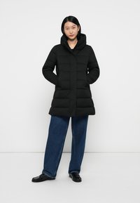 Giubbotto imbottito nero con cappuccio, dal taglio dritto, texture trapuntata e tasche laterali, abbinato a pantaloni in denim a vestibilità ampia.
