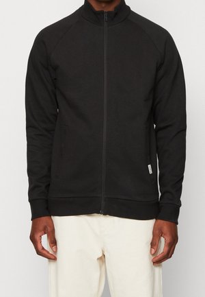 Giacca nera con zip e colletto alto, maniche raglan e tasche laterali. Realizzata in un tessuto liscio ed elasticizzato con polsini aderenti.