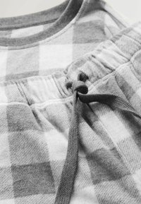 Grau-weißer karierter Stoff eines gemütlichen Kleidungsstücks, das über eine weiche Textur, einen elastischen Taillenbund und eine gebundene Kordel verfügt.