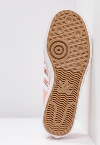 Suola di una sneaker Adidas rosa con battistrada in gomma marrone testurizzata, motivi circolari, scanalature ondulate e logo Adidas al centro.