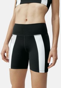 Visokotlačne črne kratke hlače z belimi stranskimi črtami, izdelane iz raztegljivega materiala. Imajo ravne šive za udobje in gladko teksturo.