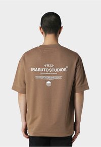 Brun oversized t-skjorte med kort erm som har hvit tekst og logo på baksiden, laget av mykt stoff med en avslappet passform.