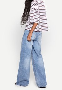 Randig, kortärmad topp i vitt och rött, kombinerad med vida ljusblå denimjeans med slitna effekter och bakfickor.