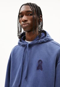 Haut à capuche bleu marine avec cordon de serrage, poche avant et logo brodé sur la poitrine. Tissu doux avec une coupe décontractée.