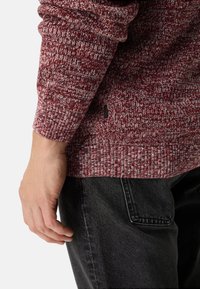 Gebreide bordeauxrode trui met gespetterde structuur; geribbelde boorden en zoom; klein logodetail aan de zijkant; gecombineerd met donkere denim jeans.