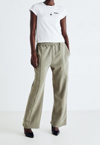 Bílá bavlněná tričko s krátkým rukávem a černým logem, spárované s volnými olivově zelenými kalhotami s elastickým pasem a třepeným okrajem.