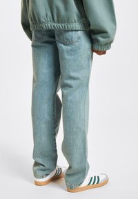 Light blue, straight-leg jeans with a soft texture. Features back pockets and a casual fit, paired with white sneakers with green accents.