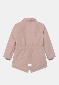 Vaaleanpunainen, pitkähihainen takki, jossa on joustava vyötärö, suppilomainen kaulus ja pyöreä helma. Selässä vyötärön lähellä on brändilogo.