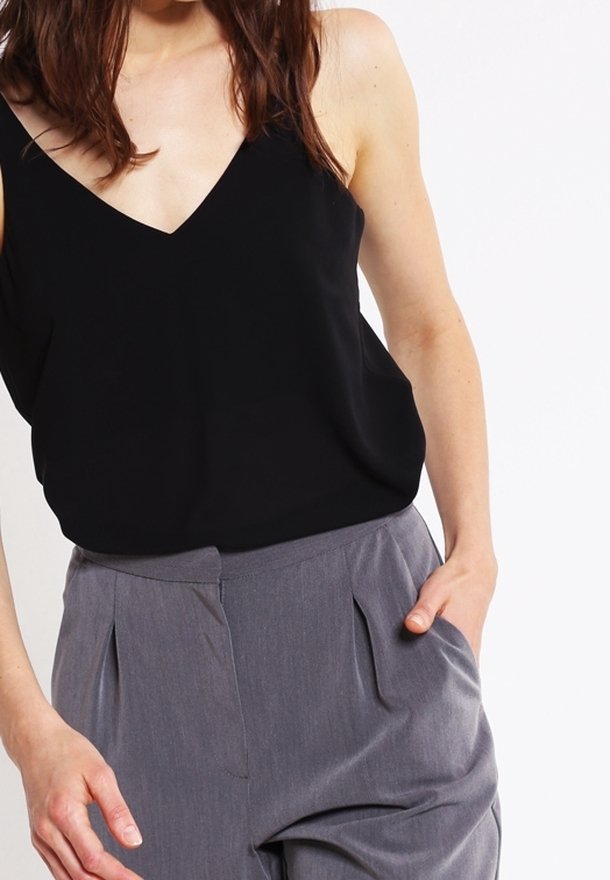 Svart ärmlös topp med V-ringning, ihopparad med grå skräddarsydda byxor med veck och sidofickor. Slät tygstruktur.