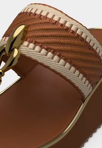 Sandalo con tacco marrone con cinturino intrecciato beige e ruggine, dettaglio a catena dorata e suola in pelle liscia.