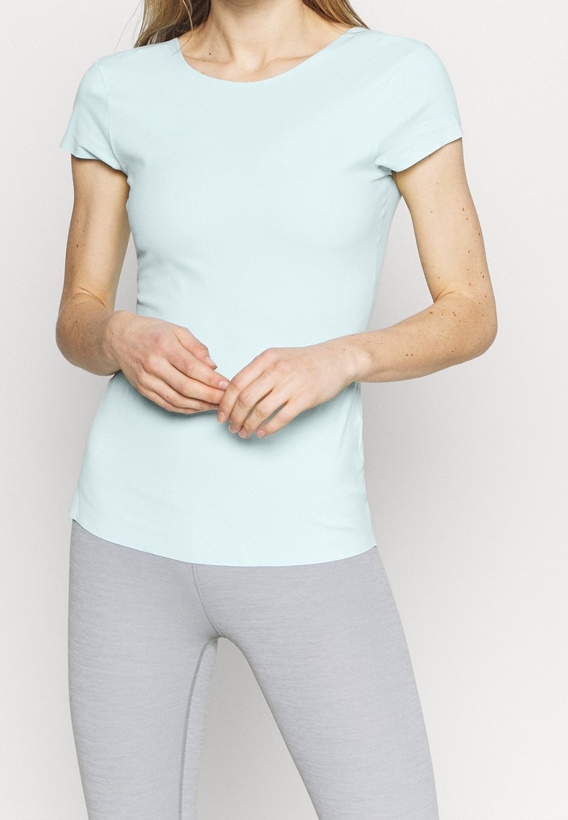 Camiseta ajustada de manga corta color azul claro, hecha de una tela suave, con un escote redondeado, combinada con unos pantalones tipo leggings de color gris claro.