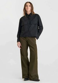 Chemise noire à boutons avec deux poches poitrine, associée à un pantalon taille haute, jambes larges, de couleur vert olive dans un tissu texturé.