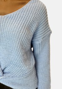 Hellblauer Strickpullover mit V-Ausschnitt, locker geschnitten, mit strukturiertem Muster und aufgeschlagenen Ärmeln. Das Material wirkt weich und atmungsaktiv.