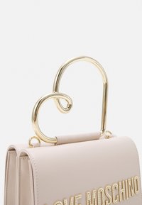 Rosa läderhandväska med ett guldmetalliskt hjärtformat handtag. Har präglad texten "LOVE MOSCHINO" på framsidan. Slät yta.