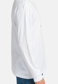 White long-sleeve shirt in cotton with a relaxed fit. Features a textured logo and text in white along the left sleeve, round neckline.
