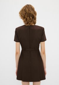 Bruine korte jurk met korte mouwen, aansluitende taille en geplooide rok. Zichtbare ritssluiting aan de achterkant en tailleband detail. Gladde stoftextuur.
