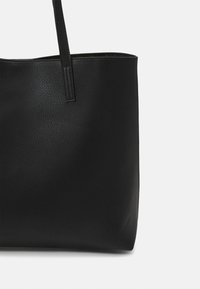 Czarna skórzana torba tote o fakturowanym wykończeniu, z jedną długą rączką i otwartym topem. Prosta, niezdobiona sylwetka.