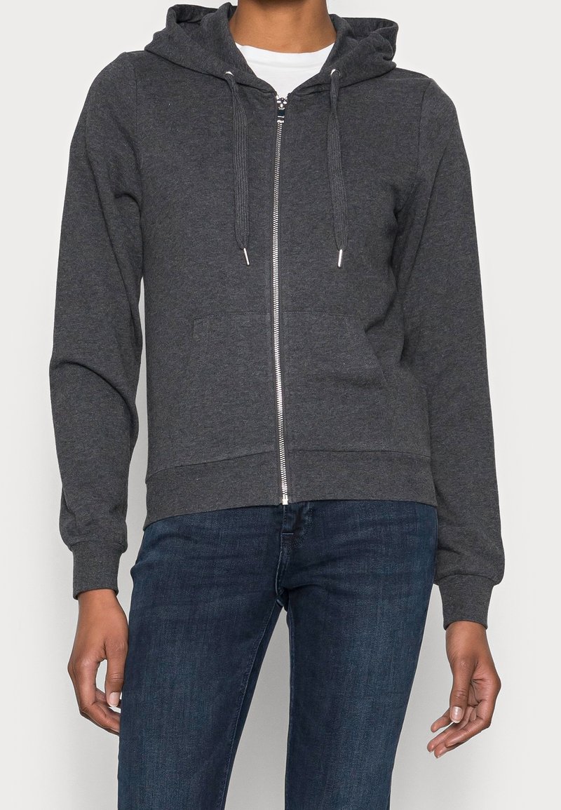 Grijze zip-up hoodie van zachte stof, voorzien van een trekkoordkap, voorkantzakken en geribde manchetten. Gecombineerd met donkere jeans.