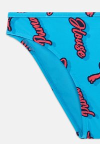 Modra bikini spodnjica z gladko teksturo, črnimi in rdečimi logotipnimi potiski ter dodanimi šivi za večjo vzdržljivost.