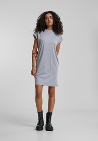 Šedé šaty s krátkými rukávy z měkké látky, volný střih, sahají nad kolena. Kombinované s černými kotníkovými botami s masivní podrážkou.