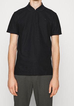 Sort polo shirt lavet af bomuld med kort lynlås i halsen, korte ærmer og et ensfarvet design med en lille logo på brystet.