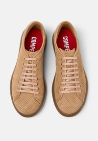 Zapatillas perforadas color marrón claro con forma redondeada, cordones planos y suelas de goma marrones. El interior cuenta con una plantilla roja con la impresión "CAMPER".