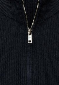 Îmbrăcăminte din tricot cu nervuri de culoare bleumarin, cu guler înalt și fermoar argintiu. Fermoarul are un tab de tragere rectangular, adăugând un accent metalic.