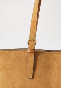 Borsa tote in suede beige con design piatto, una singola tracolla regolabile e una fibbia in metallo dorato per la regolazione della tracolla.
