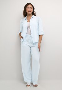 Chemise rayée bleu clair et pantalons larges assortis en tissu doux. La chemise a un devant à boutons et des manches retroussées.