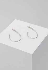 Boucles d'oreilles en argent présentant un design minimaliste ; forme allongée et courbée avec une texture lisse et une finition polie.