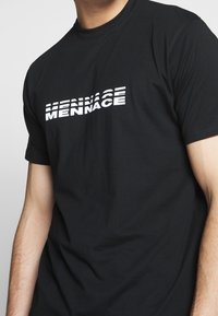 T-shirt en coton noir avec un imprimé graphique blanc affichant "MENACE" dans une police audacieuse et stylisée sur la poitrine. Manches courtes.