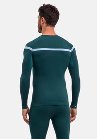 Długi rękaw sportowej bluzki w ciemnozielonym kolorze z teksturowanym wzorem, z białym poziomym paskiem na ramionach i dopasowanym krojem.