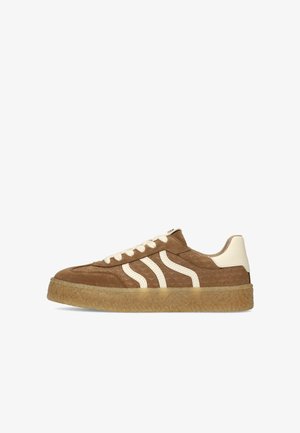 Brown suede sneaker with cream leather accents, white laces, textured gum sole, and two wavy cream stripes on side.