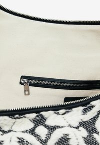 Große Textiltasche mit schwarz-weiß gemustertem Äußeren, ausgestattet mit einem glatten Reißverschluss und einer Innentasche mit silbernem Reißverschluss.