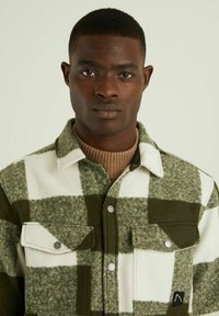 Groene en witte geruite wollen shirtjack met twee voorkruiszakken, drukknoopsluitingen en een zwart logo-accent. Zachte textuur, kraagontwerp.
