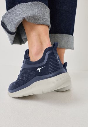 Scarpa sportiva blu navy con tomaia in mesh testurizzato, suola grigia a contrasto e linguetta sul tallone. Presenta un design elegante e arrotondato.