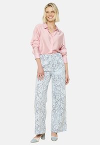 Lichtroze blouse met knopen gecombineerd met wijde, lichtblauwe kanten broek. De outfit heeft een ontspannen pasvorm en subtiele gestructureerde patronen.