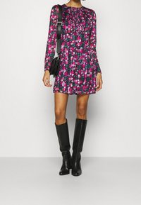 Mini mekko kukkakuviolla, jossa on pitkät hihat ja rypistynyt kaula-aukko, sävyissä vaaleanpunainen ja vihreä. Yhdistetty polven korkeisiin mustiin nahkasaappaisiin.