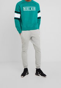 Teal Nike Air sweatshirt med vita och svarta ränder, kombinerad med grå joggers och svarta sneakers. Enkel, avslappnad atletisk stil.